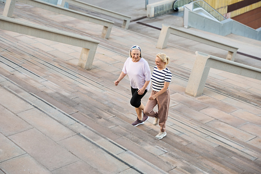 Cheerful senior women in sneakers climbing stairs