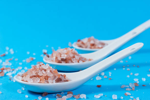 Close-up of ceramic teaspoons with pink Himalayan salt on blue background.
