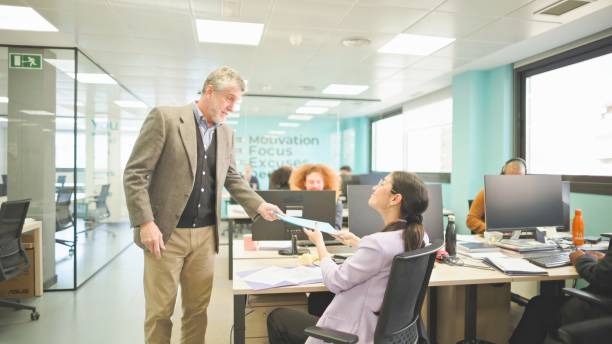 istock Businessman and woman exchanging documents in a lively office. 2148759500