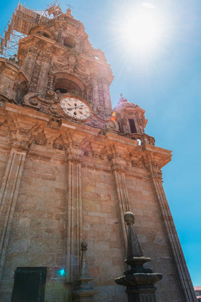 The sun casts a heavenly glow over the historic Cathedral of Santiago de Compostela, illuminating its intricate facade and clock tower against a vibrant blue sky.