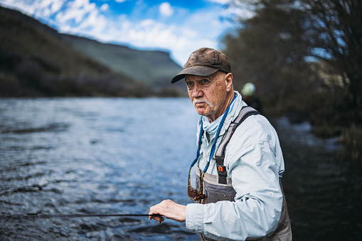 A retired senior man of Caucasian descent with a focused expression fly fishes in Central Oregon on a beautiful Spring day.