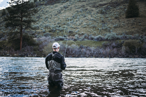 Cropped view of a Caucasian man wearing waders fly fish on the Deschutes River during a weekend trip to Central Oregon.