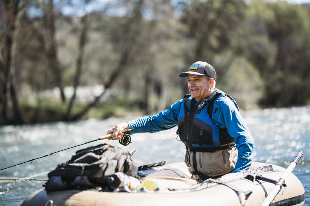 A smiling middle aged Caucasian man leans out of an inflatable fishing boat while fly fishing on a beautiful Spring weekend in Central Oregon.