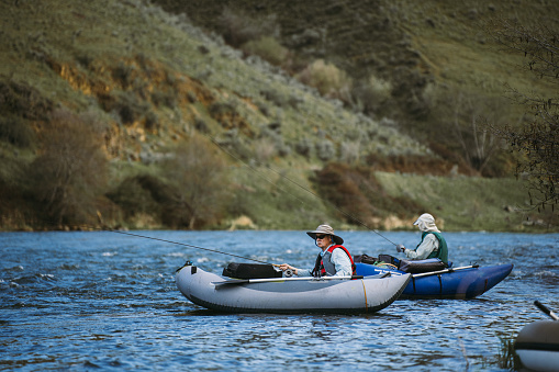 Two active senior men on a fly fishing trip together in Central Oregon sit in inflatable boats while fishing in the Deschutes River.