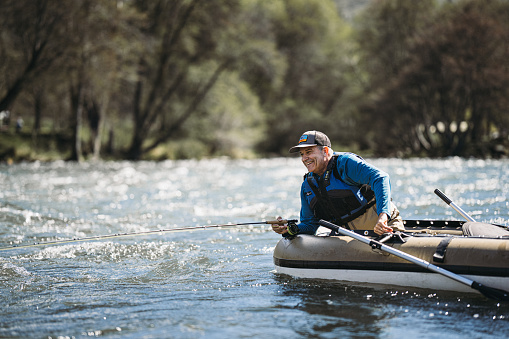 A smiling middle aged Caucasian man leans out of an inflatable fishing boat while fly fishing on a beautiful Spring weekend in Central Oregon.