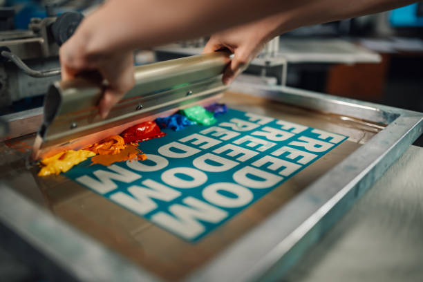 istock Close up of graphic worker's hands using squeegee for screen printing. 2148765777