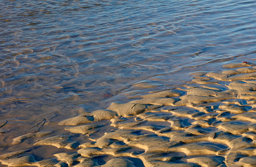 Sunlit ripples wash up on the textured sand of a tide pool in Newport Beach