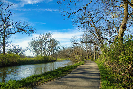 Sunny Spring landscape of the Illinois Michigan Canal Towpath Trail curving beside calm canal waters passing forests and fields near Rockdale, Illinois.
