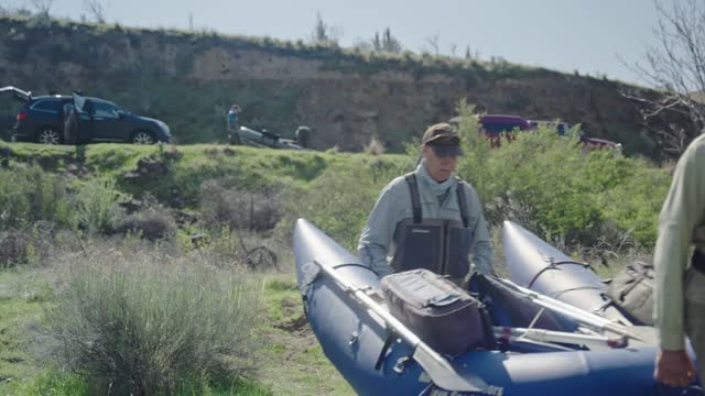 Active senior men on fishing trip carrying inflatable boat to the river