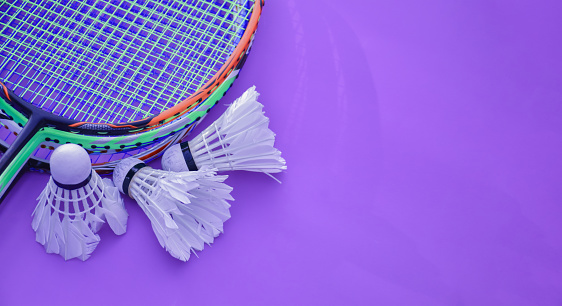 Badminton rackets and white cream shuttlecocks on violet floor.