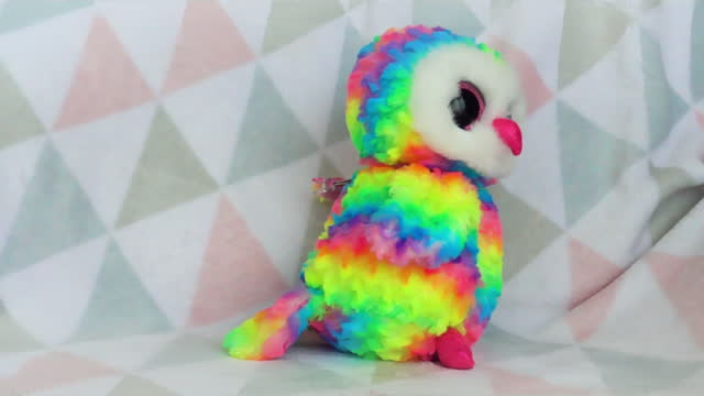 Stuffed and fluffy plush and rainbow toy owl fall on a soft baby blanket. Slow motion.