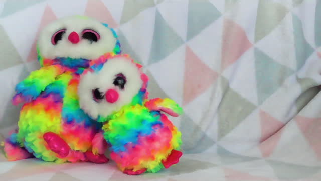 Stuffed and fluffy plush and rainbow toys owls fall on a soft baby blanket. Slow motion.