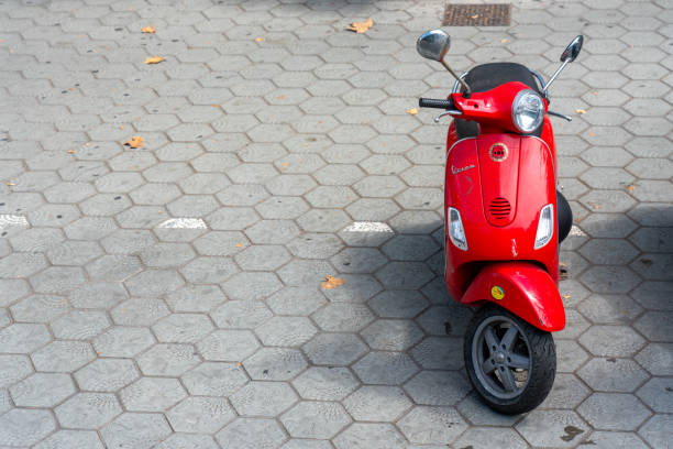 Valencia, Spain - August 10, 2025: Side view of red motor scooter parked next to bus stop in the city of Valencia, Spain. This is a very used alternative to cars to move quickly and efficiently all around the city