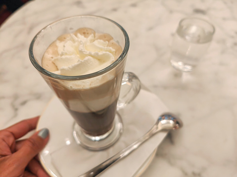 Close- up shot of unrecognizable person drinking Einspänner coffee (An espresso topped with whipped cream (Schlagobers) and served in a glass )