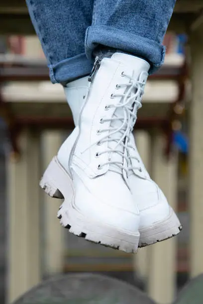 Photo of Crossed female legs in white  boots and blue rolled jeans . Vertical shot