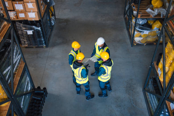 istock Three warehouse workers, wearing safety vests and helmets, discuss operational details in a busy, well-stocked industrial warehouse, emphasizing safety and teamwork. 2148771370