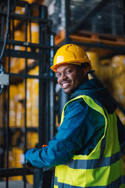 istock A confident and cheerful male warehouse worker wearing a yellow hard hat and reflective safety vest stands in a well-organized industrial warehouse. 2148771412