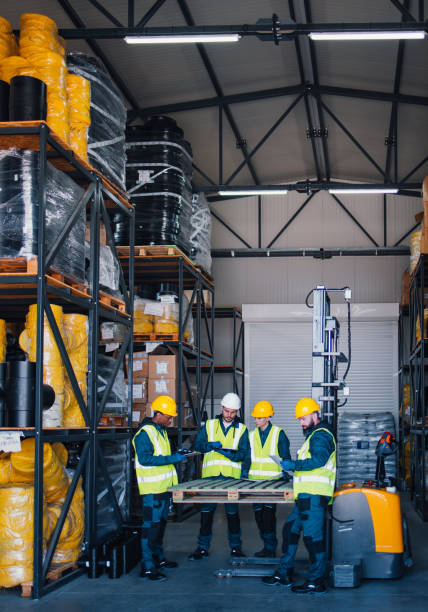 istock A diverse group of workers wearing safety gear engaging in a discussion within a well-organized industrial warehouse. The scene depicts teamwork and effective workplace safety practices. 2148771424