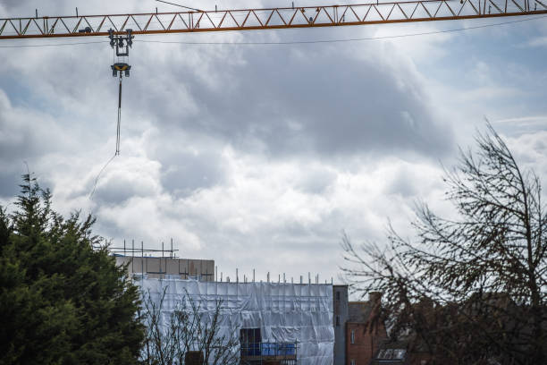 istock Construction crane above flame retardant scaffold sheeting wrapped apartments building during insulation in england uk 2148771976