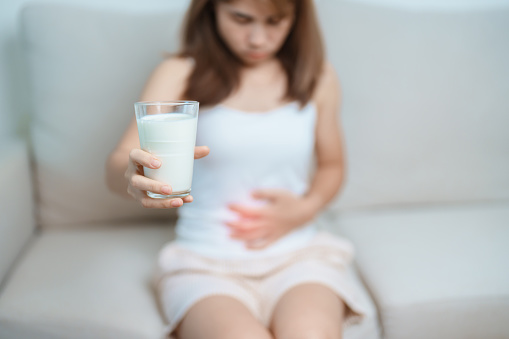 Lactose intolerance and Milk allergy concept. woman hold Milk glass and having abdominal cramps and pain when drink Cow Milk. Symptom stomach ache, Dairy intolerant, Nausea, Bloating, Gas and Diarrhea