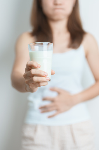 Lactose intolerance and Milk allergy concept. woman hold Milk glass and having abdominal cramps and pain when drink Cow Milk. Symptom stomach ache, Dairy intolerant, Nausea, Bloating, Gas and Diarrhea