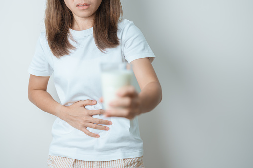 Lactose intolerance and Milk allergy concept. woman hold Milk glass and having abdominal cramps and pain when drink Cow Milk. Symptom stomach ache, Dairy intolerant, Nausea, Bloating, Gas and Diarrhea