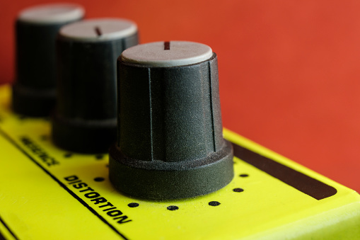 Macro image of electric guitar pedal. Only a knob and the word distortion is on focus. Red background. Analog and vintage gear, old-fashioned hobbies and jobs. No-digital sounds.