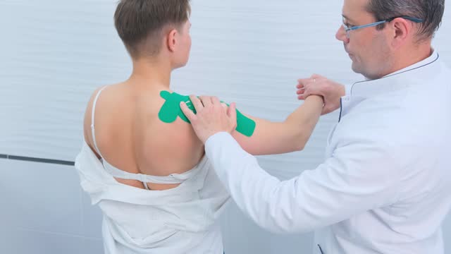 An orthopedic traumatologist examines the patient's shoulder joint and checks the mobility of movements in the office.