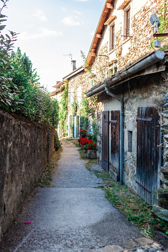 A quaint alleyway flanked by rustic stone houses with wooden shutters and blooming red flowers captures the essence of a serene European village. Yvoire