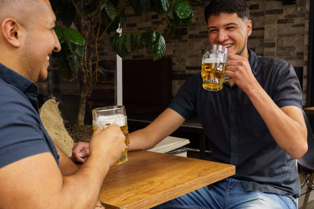 istock Two men are sitting at a table, both holding glasses of beer 2148777403