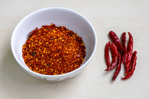 Dried chili flakes in a bowl on a wooden background, also known as crushed red pepper flakes.
