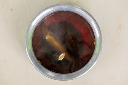 Freshly brewed black tea or red in a silver bowl with steam on wooden background. Cinnamon, cardamom, and bay leaves are used to make this healthy tea. In Bangladesh, it is called Rong Cha or Lal Cha.