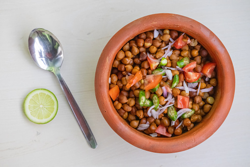 Boiled chickpeas in an earthen pot on wooden background. Chopped tomatoes, onion, and green chilies mixed with Bengal gram. Healthy weight loss meal. Locally in Bangladesh, it is called Chola Boot.