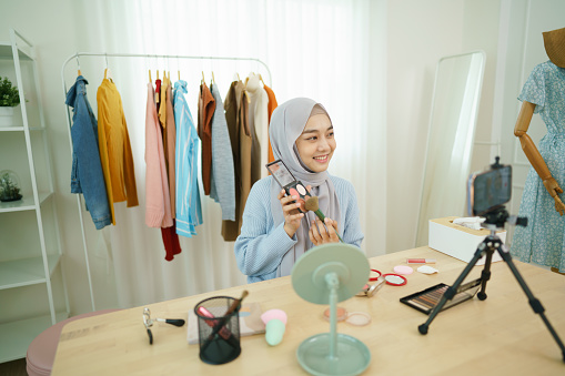 Beautiful Muslim girl lives streaming on social media platform story selfie cosmetic makeup demonstration at home. Muslim woman blogger teaching makeup to record videos from a smartphone.