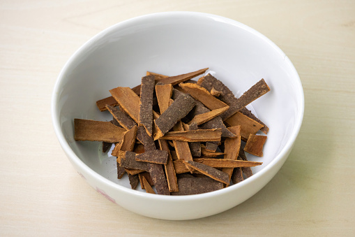 A pile of cinnamon sticks (Cinnamomum verum) in a white bowl on a wooden background. It is also known as darchini, daruchini, and dalchini.