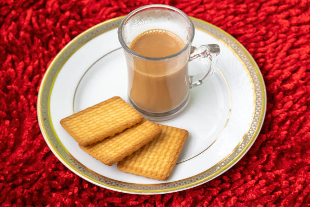 istock A cup of hot milk tea in a glass cup with biscuits on a white plate on a red carpet textured background. 2148781235