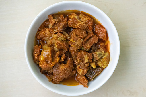 Delicious beef curry in a bowl on wooden textured background. Beef bhuna is a popular, flavorful, and spicy Bangladeshi dish. Top view.