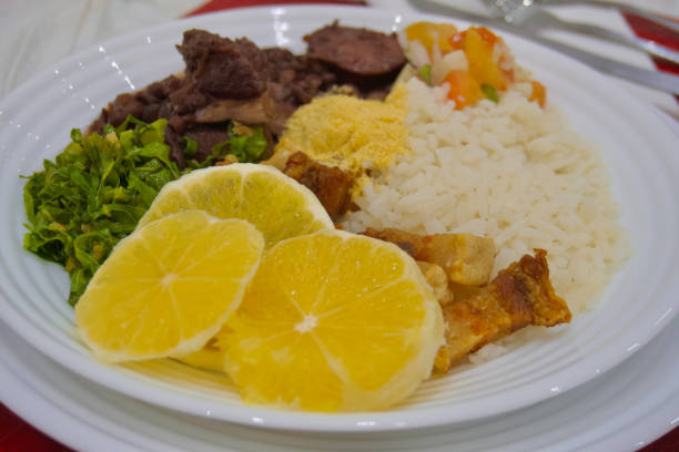 フェイジョアーダを盛り付ける白い皿のクローズアップ。オレンジスライス、米、黒豆、ソーセージ、肉などが材料です。