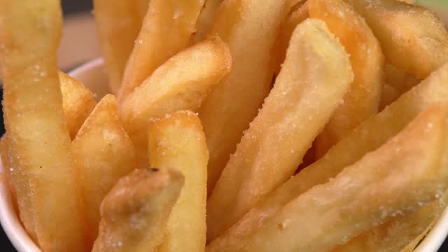 Deep fried french fries rotate on black background. Footage can be used to advertise fast food restaurants, takeaway junk food, roadside cafes, on a display in a supermarket, food truck or kiosk