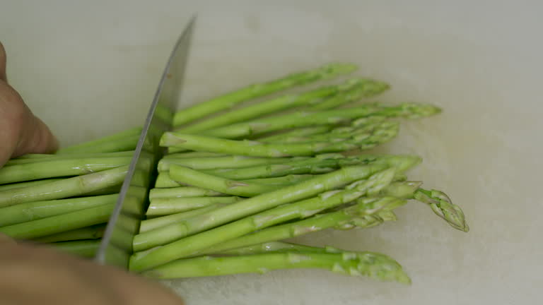 Close up, Hand of man using stainless steel knife cutting asparagus.