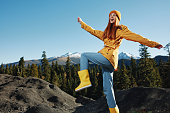 Woman smile with teeth happiness and laughter hiker in yellow raincoat put her hands up and jumping trip in the fall and hiking in the mountains in the sunset freedom