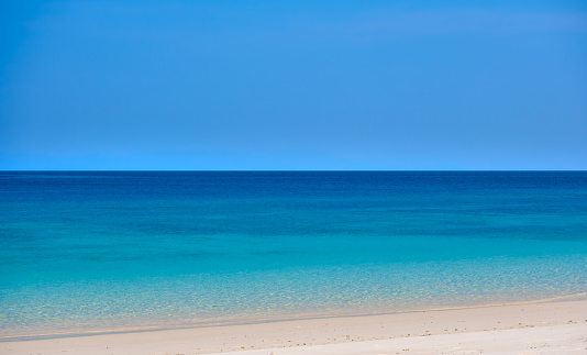 Beach sand background for summer vacation concept. Beach nature and summer seawater with sunlight light sandy beach Sparkling sea water contrast with the blue sky.