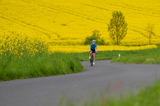 A young professional cyclist rides a bicycle quickly against the backdrop of blooming yellow rapeseed. The concept of active life, relaxation, travel, energy, sports, speed