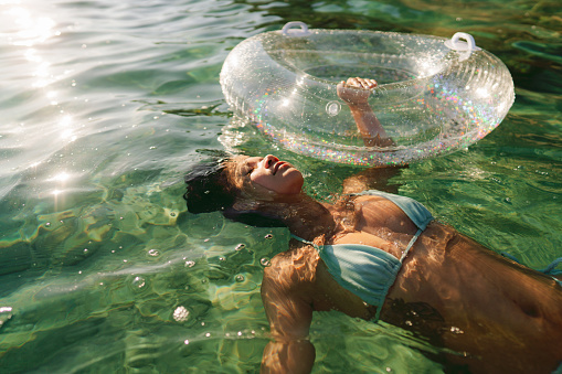 Photo of an Asian woman relaxing and cooling off in the ocean on a hot summer afternoon, using the inflatable ring