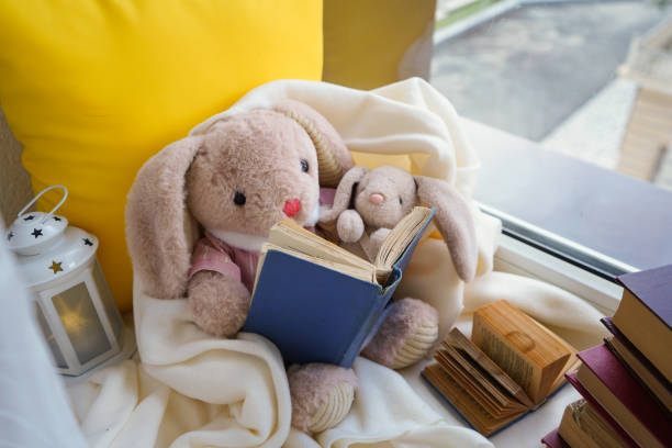 A toy hare is reading a book to a child sitting on a window in a white plaid