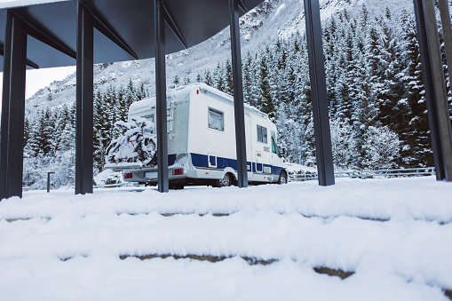 An RV stands surrounded by the serene beauty of a snow-laden mountain forest, a perfect winter escape.