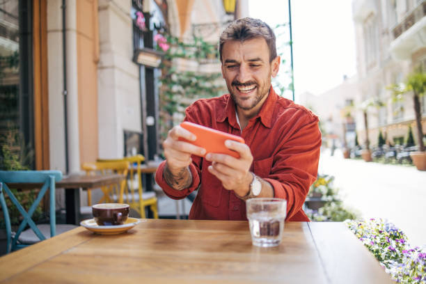 istock Man playing video games on smartphone at coffee shop 2148789699