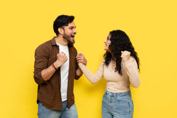 istock Happy Couple Celebrating Success on Yellow Background 2148790060