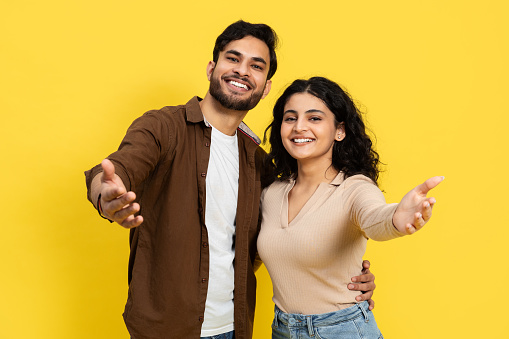 Happy Couple Embracing And Reaching Out Towards The Camera On A Yellow Background