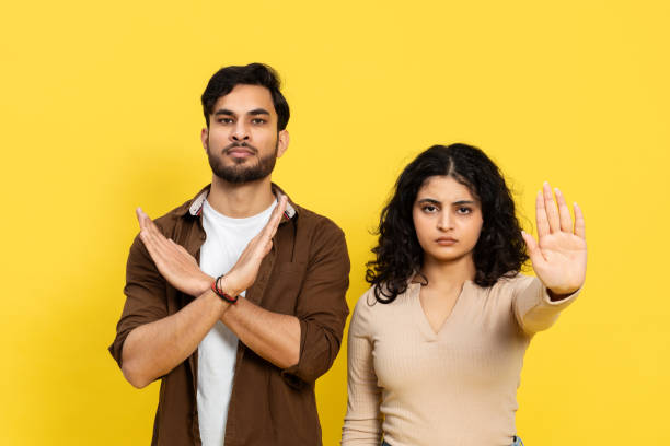 istock Confident Young Couple Gesturing Stop Sign on Yellow Background 2148790107
